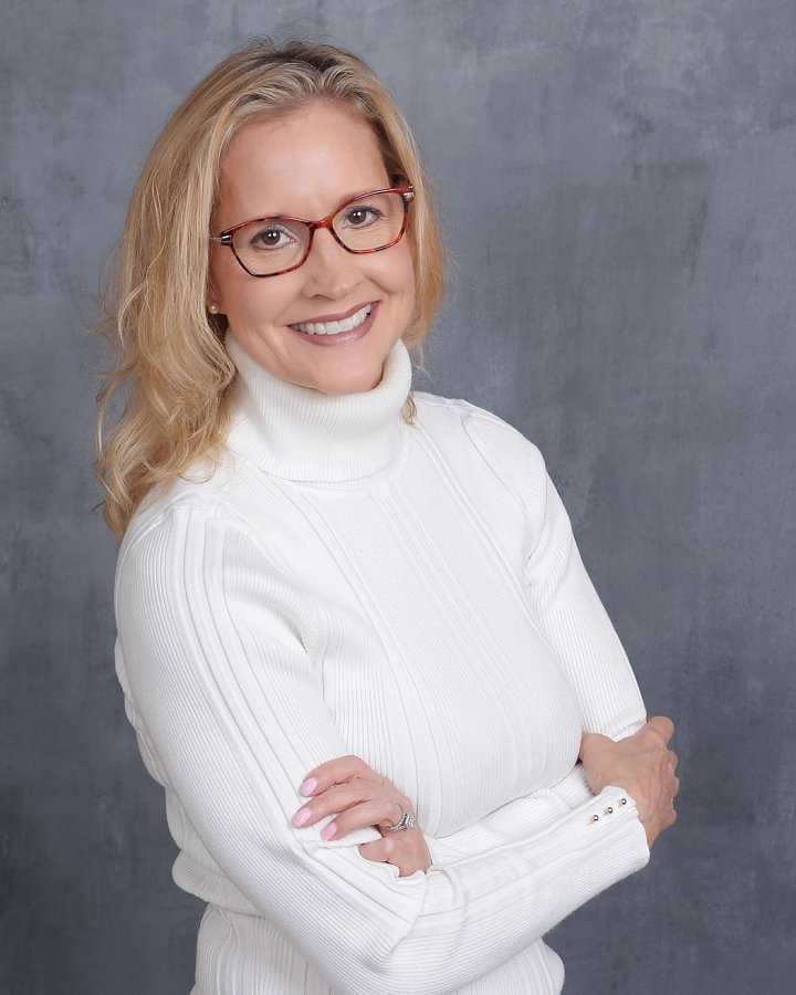 A woman in white sweater standing with her arms crossed.